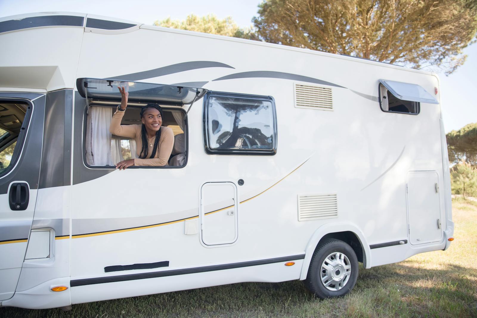 A woman smiles from a motorhome window during a sunny road trip in Portugal.