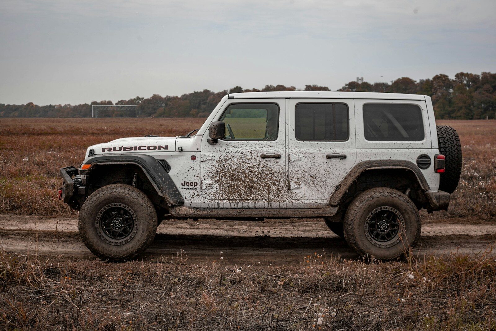 Mud-splattered white jeep wrangler rubicon on a dirt trail.